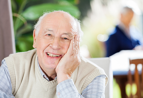 Elderly man smiling with his head resting in his right hand